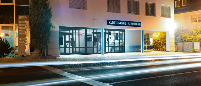 Aussenansicht des beleuchteten Eingangsbereichs der Klosterring Apotheke in Villingen, nachts, Straßenverkehr