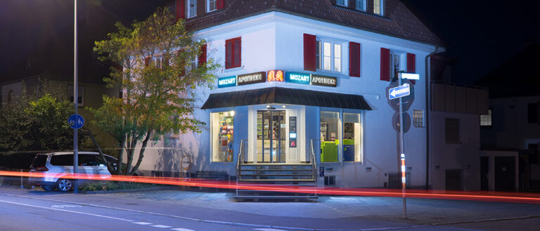 Aussenansicht des beleuchteten Eingangsbereichs der Mozart Apotheke in Villingen, nachts, Straßenverkehr
