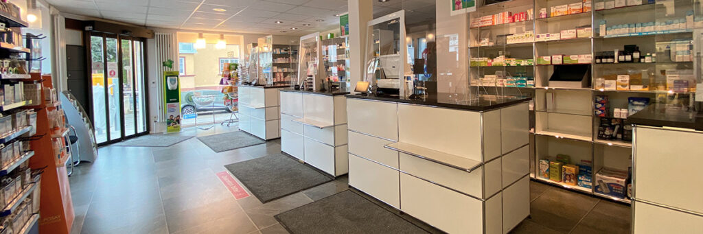 Innenansicht Verkaufsraum Mozart-Apotheke, hohe Wandregale mit Arzneimitteln in länglichem Raum, davor mehrere Verkaufstresen
