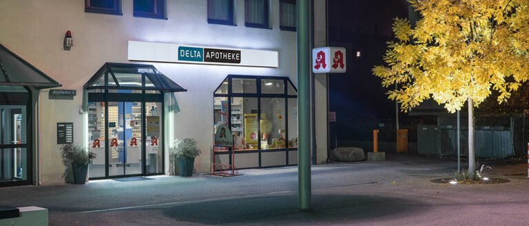 Aussenansicht des beleuchteten Eingangsbereichs der Delta Apotheke in Villingen, nachts, Straßenverkehr